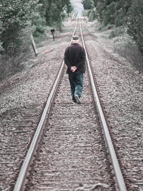 A man strolls down a single railway line, clearly following the only available route. We see him from behind, his hands clasped behind his back