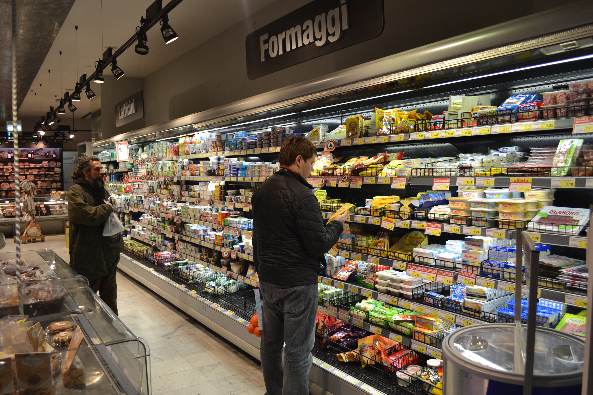 A man stands in front of a chiller cabinet in a supermarket. Above his head the sign reads Formaggi